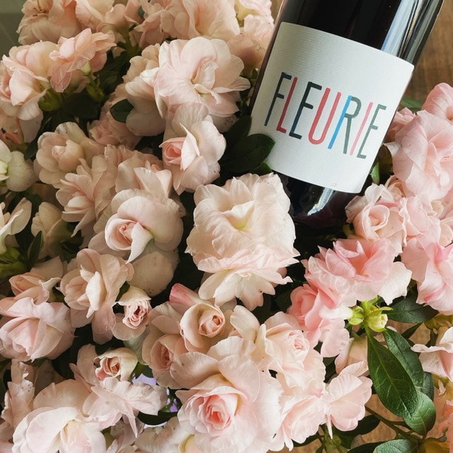 Fleurie wine bottle nestled among pink roses.