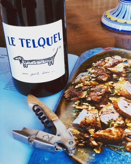Le Telquel wine bottle with dachshund label alongside charcuterie.